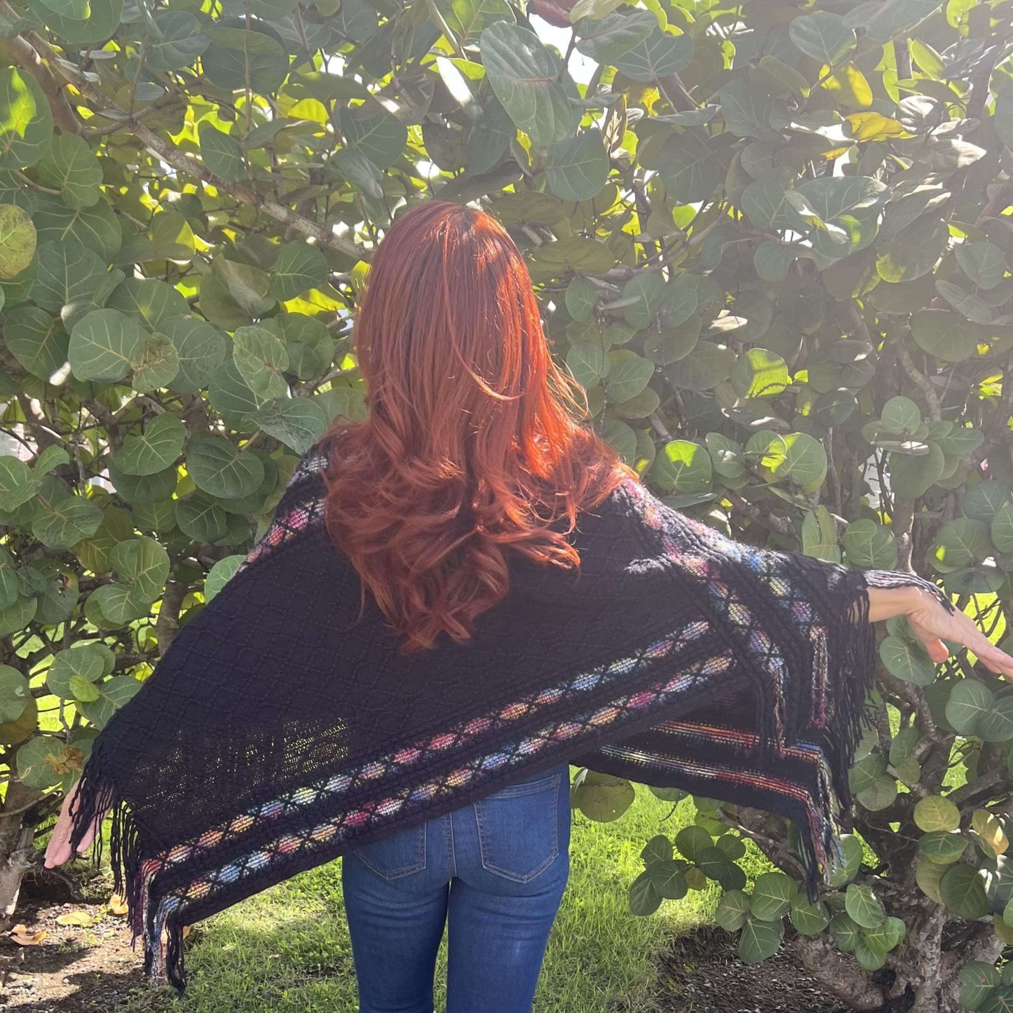 Mujer de Espaldas Mostrando Parte Trasera de un Poncho Pashmina Frente a una Arbusto de Uvas/Pololena & Co.